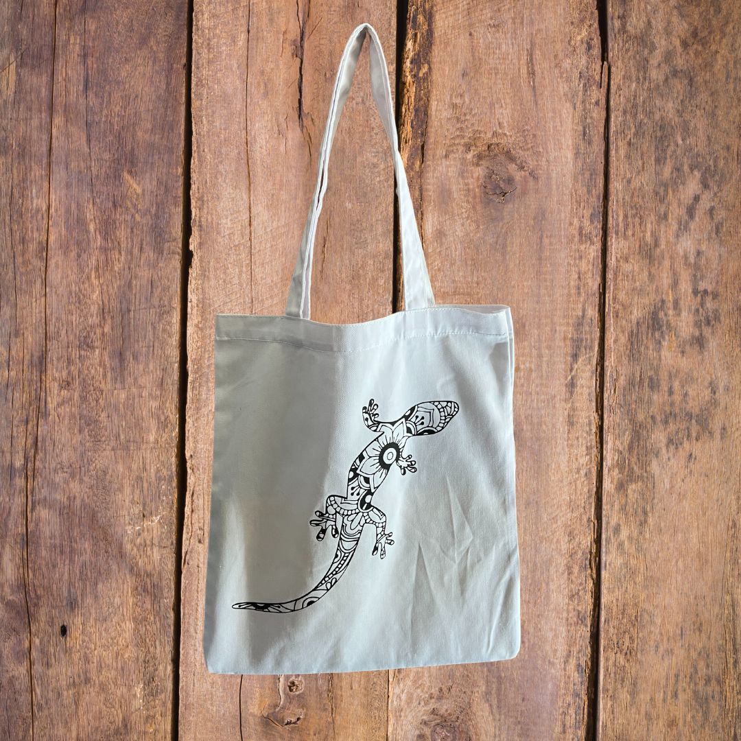 Tote bag blanc avec un lézard noire posé sur un fond en bois.